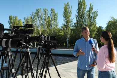 Photo of Young journalist interviewing man near river on sunny day