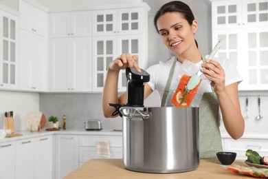 Photo of Woman putting vacuum packed salmon into pot and using thermal immersion circulator at table in kitchen. Sous vide cooking
