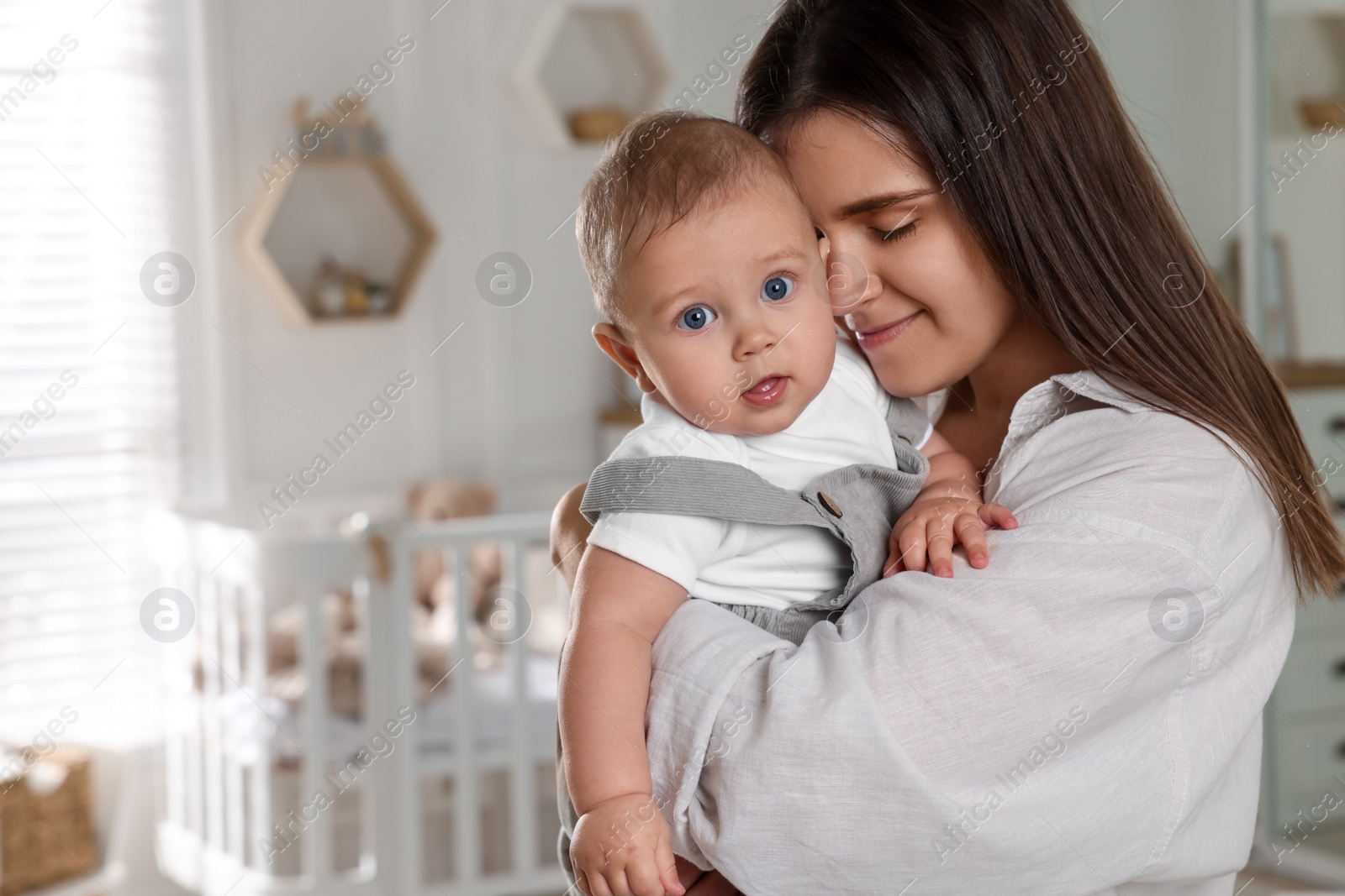 Photo of Happy young mother with her baby in nursery. Space for text