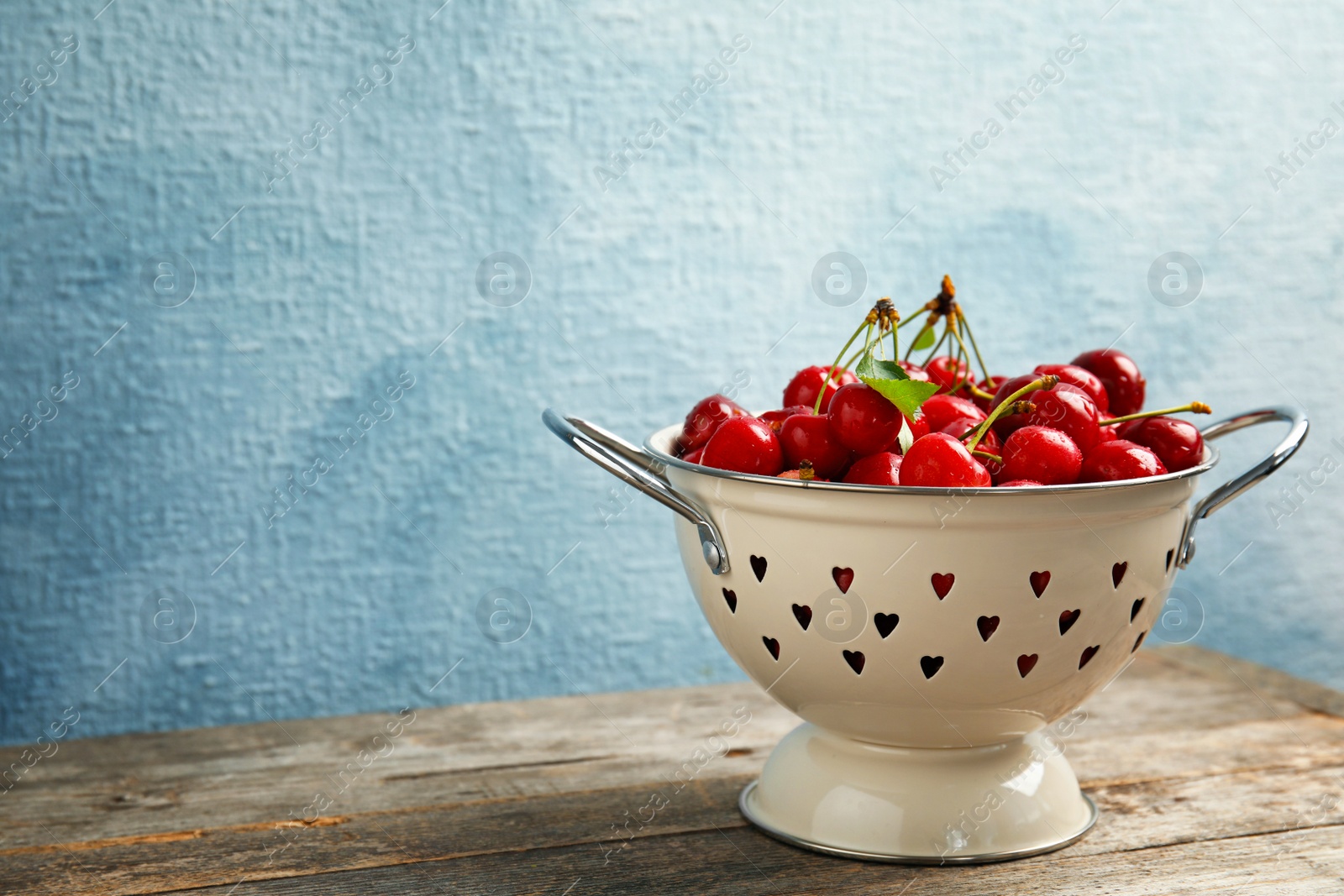 Photo of Colander with sweet red cherries on wooden table