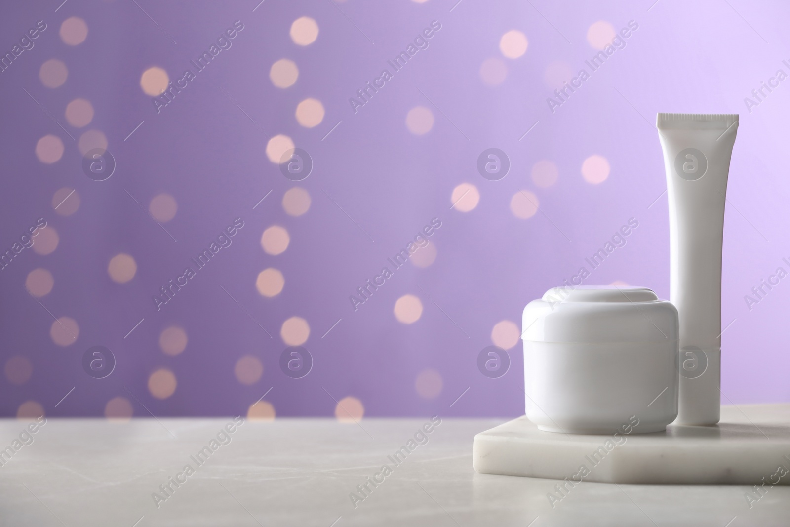 Photo of Skin care products on light table against blurred lights, space for text