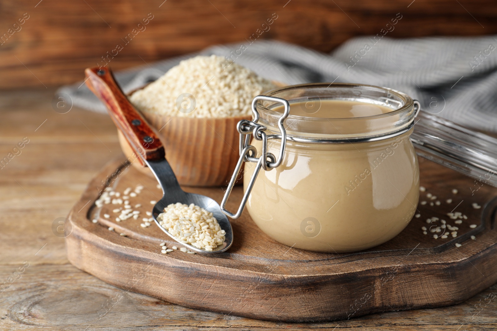 Photo of Jar of tasty sesame paste and seeds on wooden table