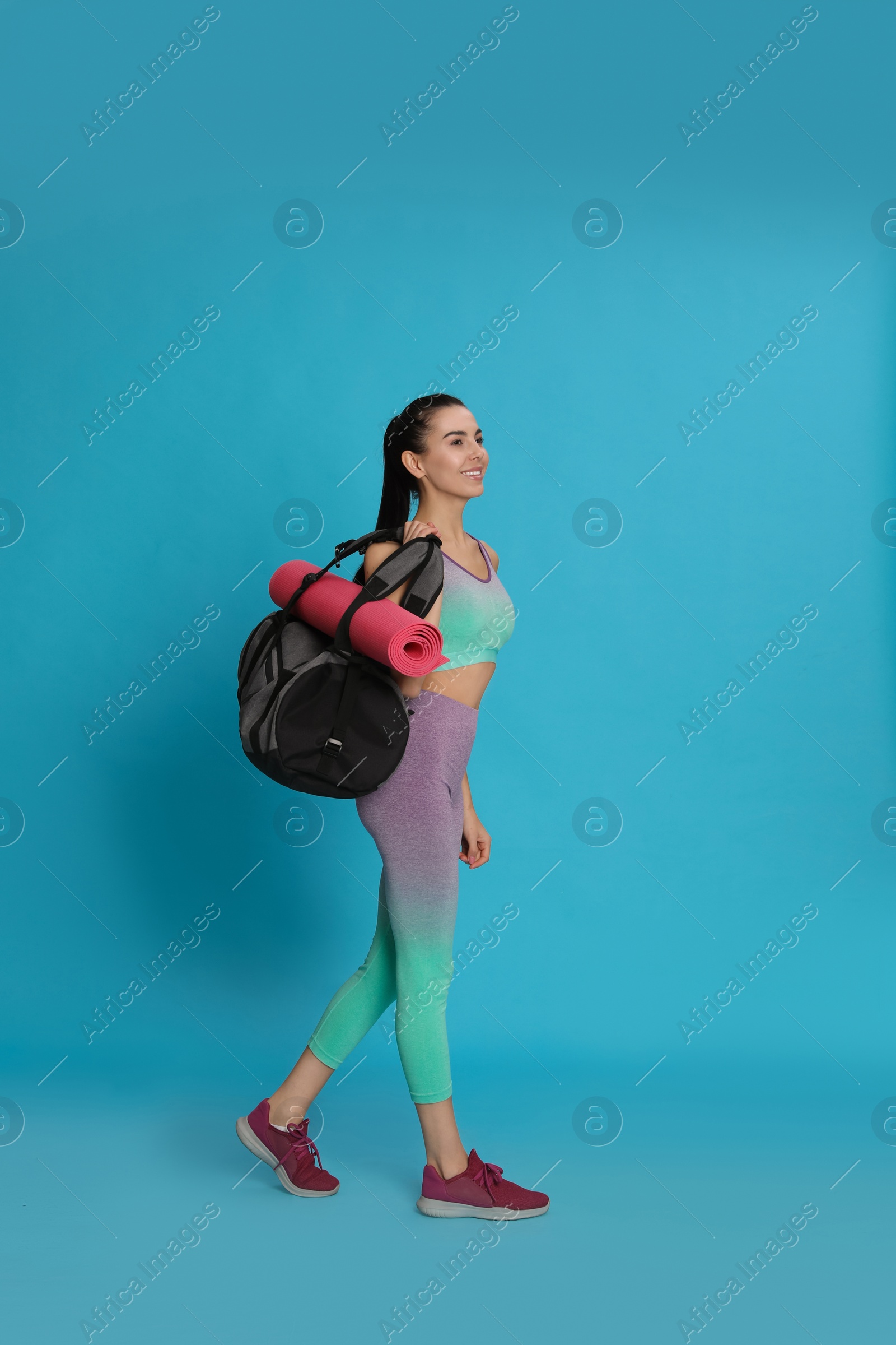 Photo of Beautiful woman with sports bag and yoga mat on light blue background