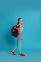 Photo of Beautiful woman with sports bag and yoga mat on light blue background