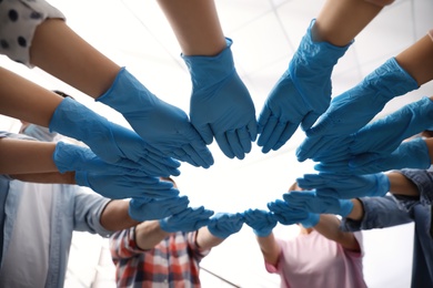 Photo of People in blue medical gloves joining hands on light background, low angle view