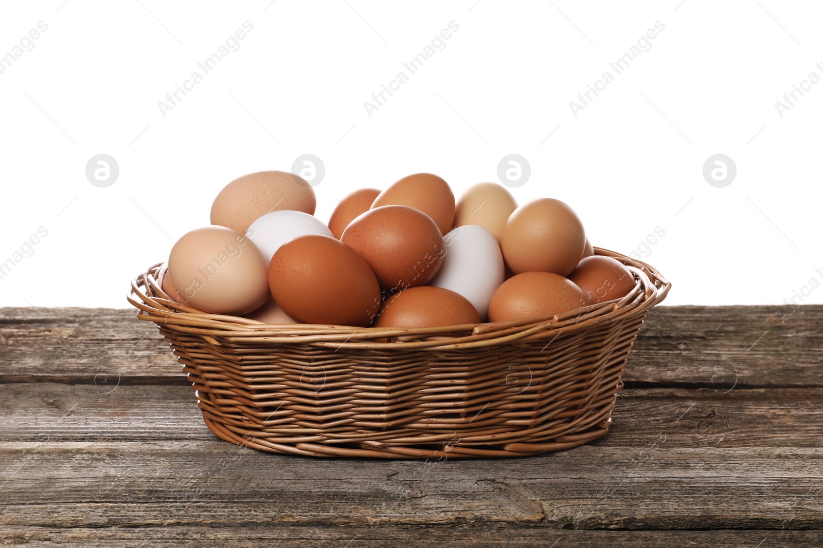 Photo of Fresh chicken eggs in wicker basket on wooden table against white background