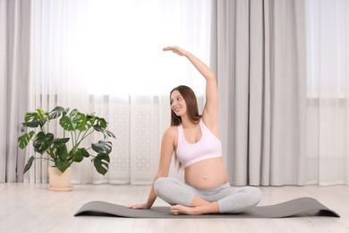 Pregnant woman doing exercises on yoga mat at home