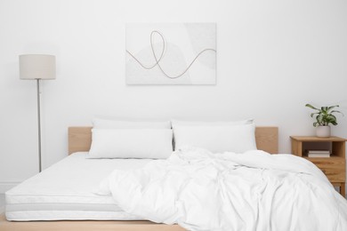 Wooden bed with soft white mattress, blanket and pillows in cozy room interior