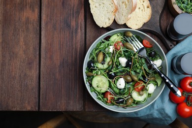 Photo of Fresh salad with vegetables, capers and mozzarella in bowl on wooden table, flat lay. Space for text