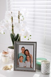 Photo of Framed family photo and orchid flower on white table indoors