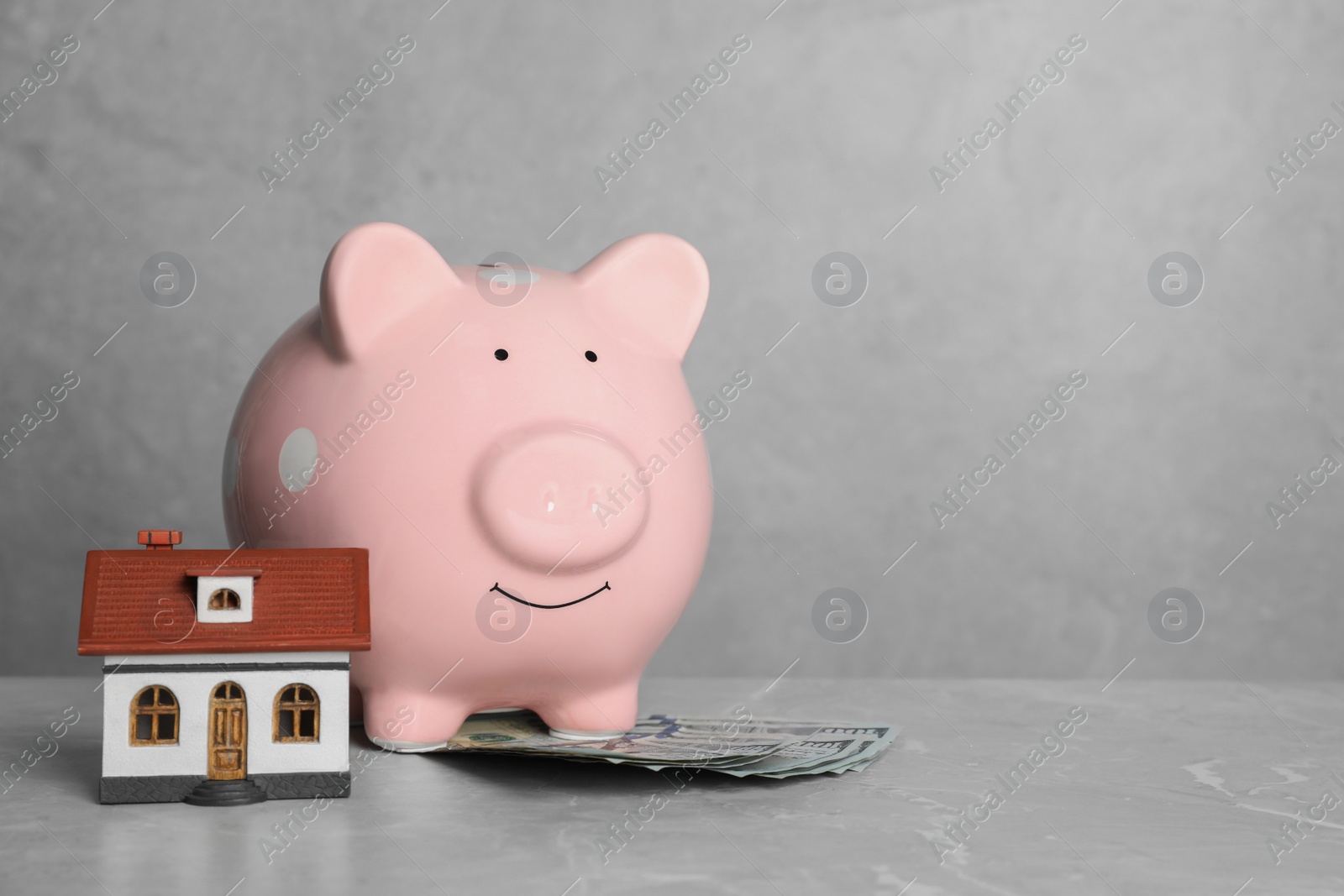 Photo of Piggy bank, dollar banknotes and house model on grey marble table. Space for text