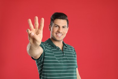 Photo of Man showing number three with his hand on red background