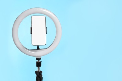 Photo of Modern tripod with ring light and smartphone on light blue background. Space for text