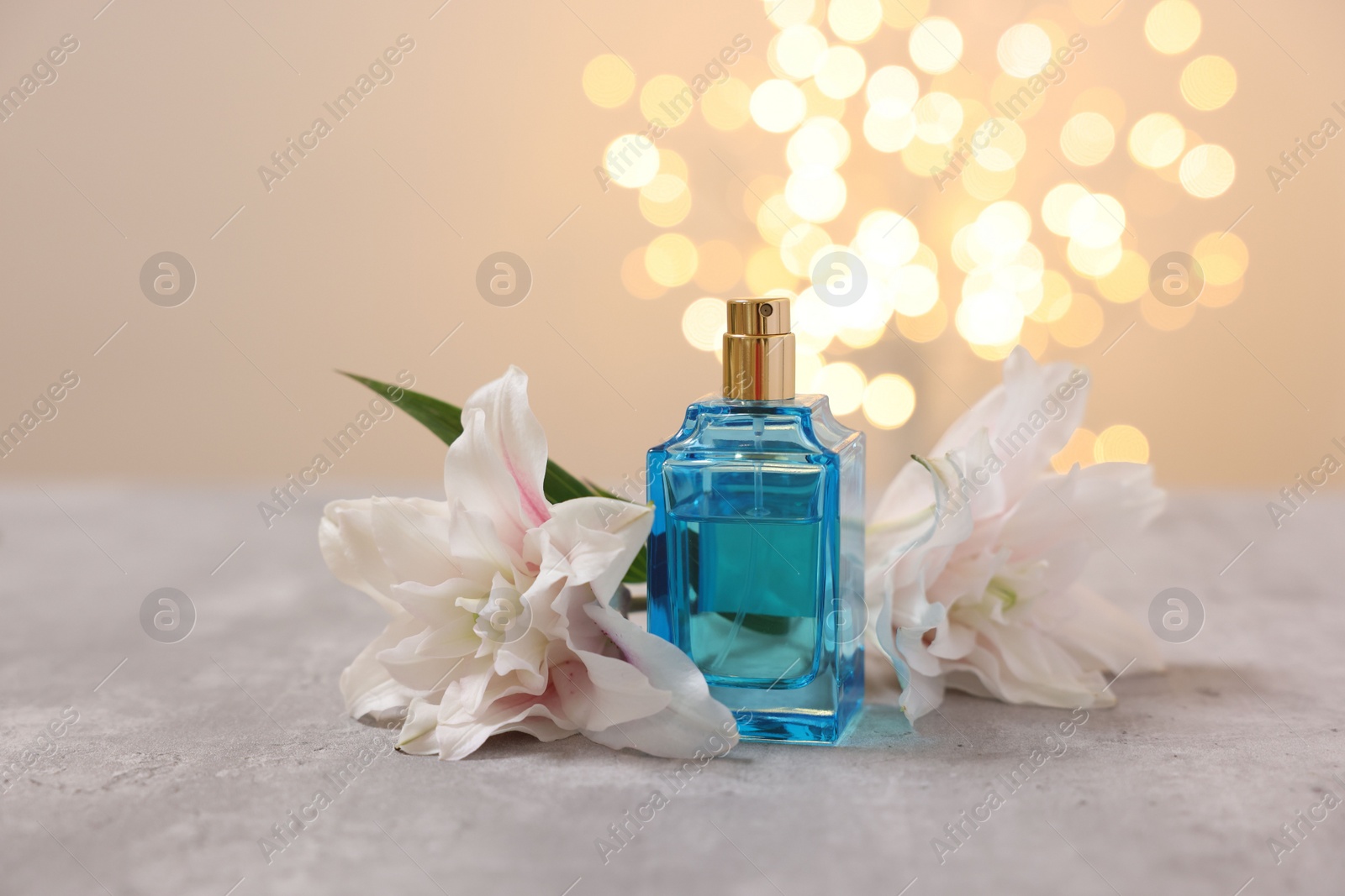 Photo of Bottle of perfume and beautiful lily flowers on table against beige background with blurred lights