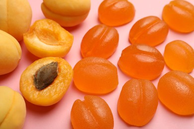 Photo of Delicious gummy apricot candies and fresh fruits on pink background, closeup