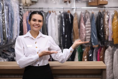 Photo of Dry-cleaning service. Happy worker near counter indoors