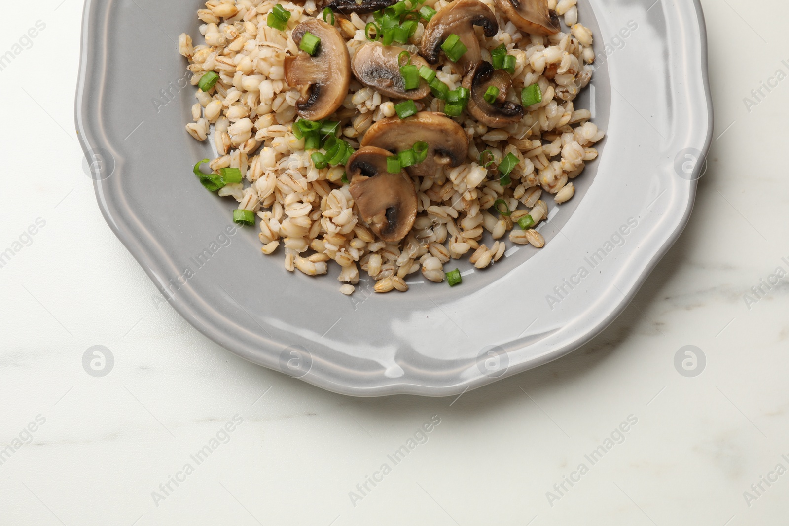 Photo of Delicious pearl barley with onion and mushrooms on white marble table, top view