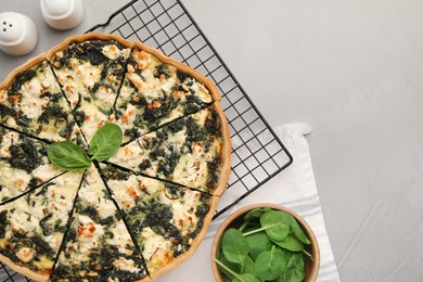 Delicious homemade quiche and fresh leaves on light gray table, flat lay. Space for text