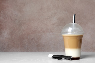 Photo of Plastic cup of tasty caramel macchiato on table, space for text