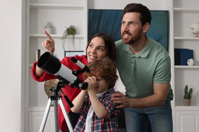 Happy family looking at stars through telescope in room