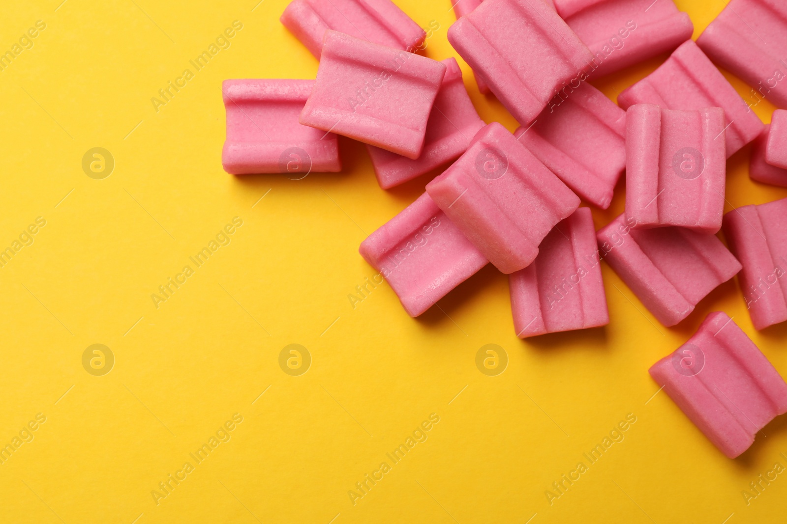 Photo of Tasty pink chewing gums on yellow background, flat lay. Space for text