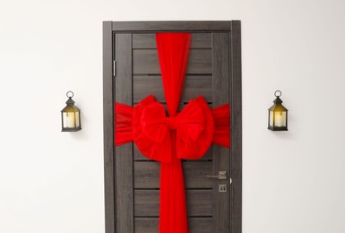 Photo of Wooden door with beautiful red bow and lanterns hanging on wall. Christmas decoration