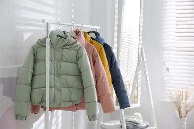 Photo of Different warm jackets hanging on rack indoors