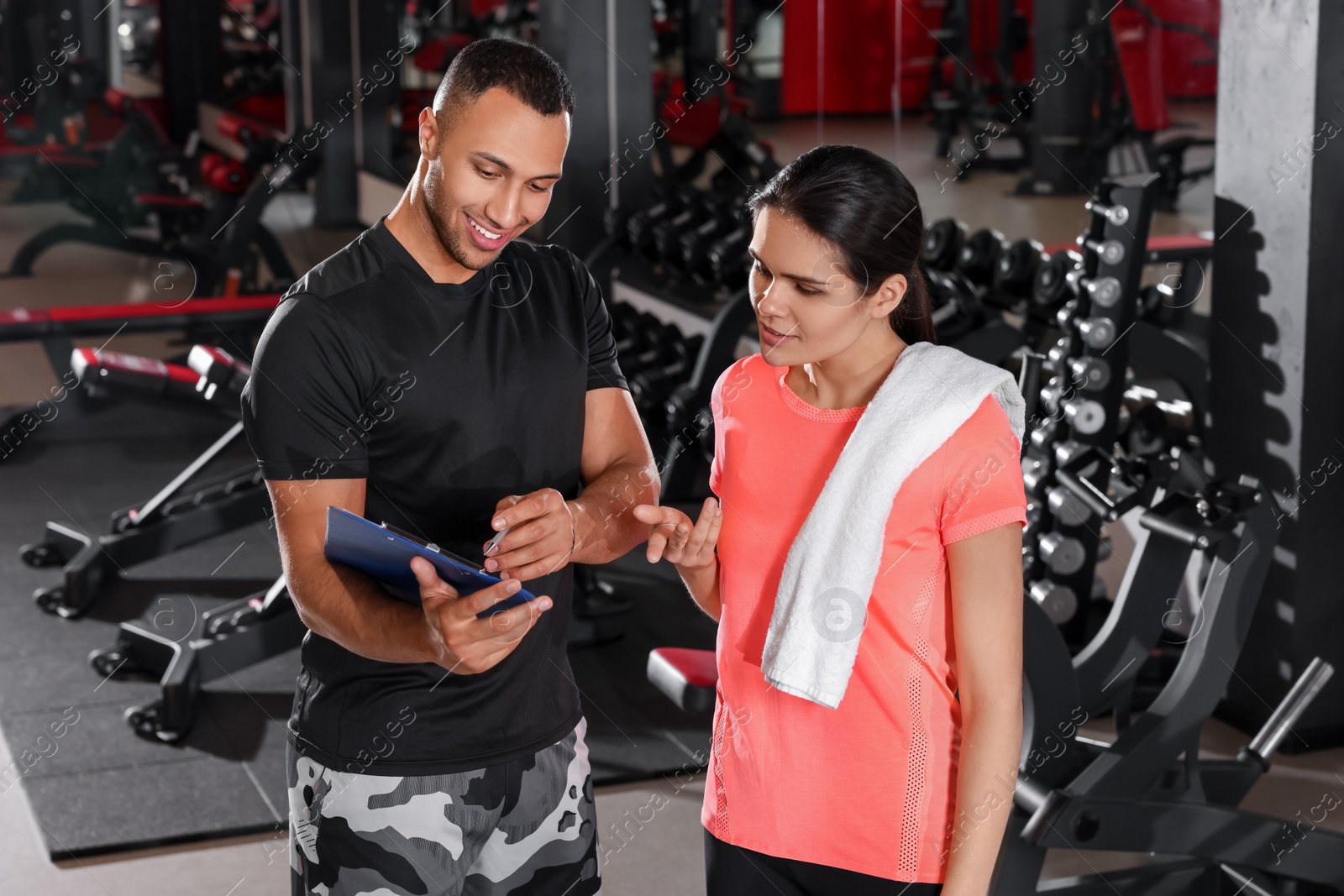 Photo of Happy trainer showing young woman workout plan in modern gym