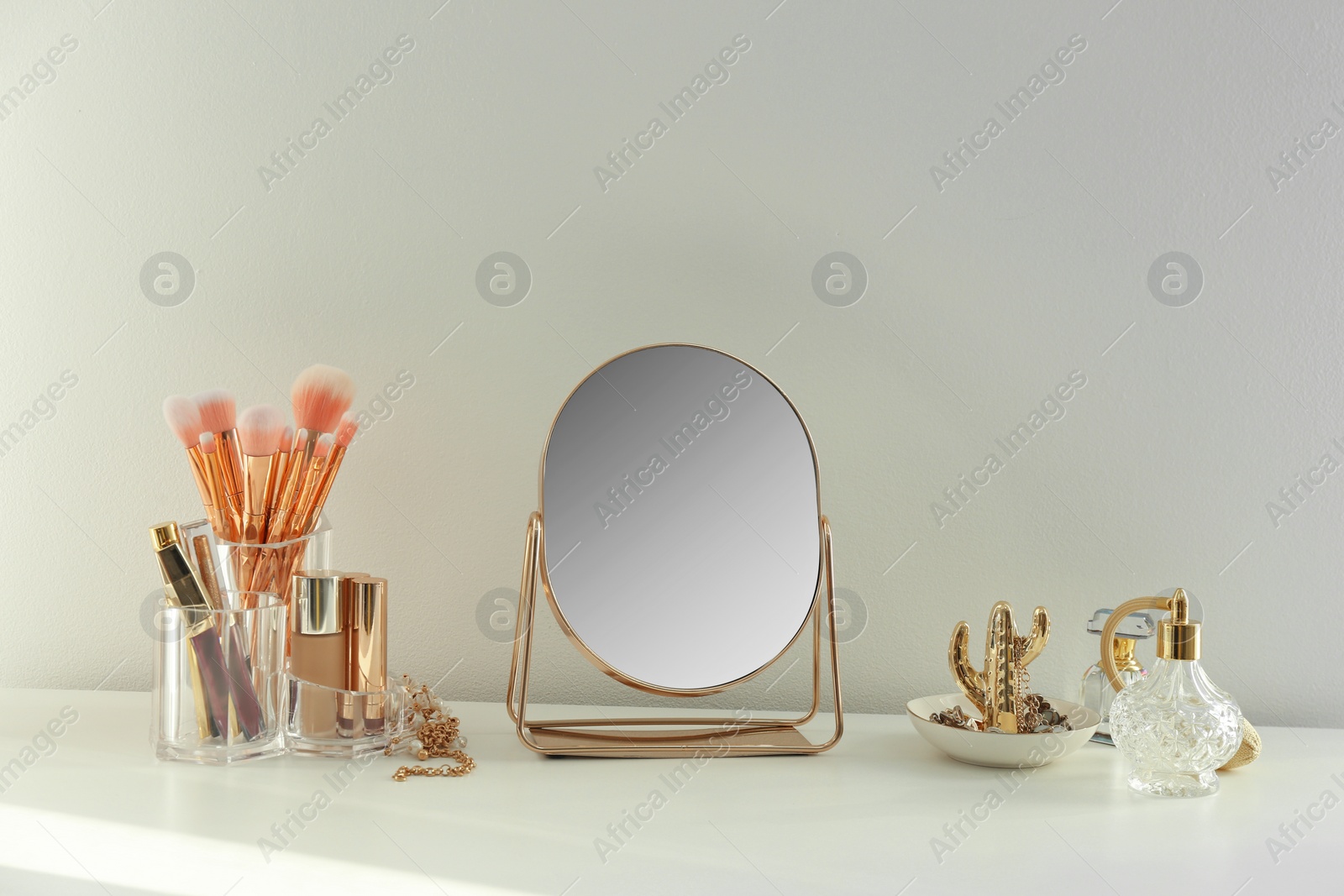 Photo of Small mirror and makeup products on white dressing table indoors