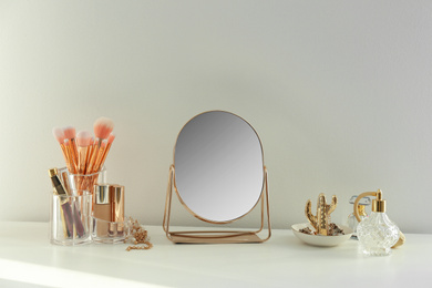 Small mirror and makeup products on white dressing table indoors