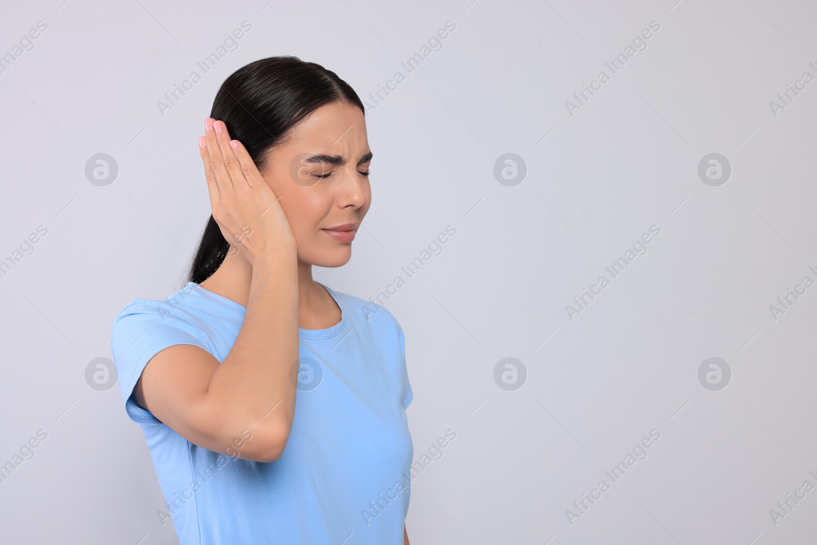 Photo of Young woman suffering from ear pain on light grey background. Space for text