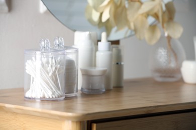 Photo of Containers with cotton swabs and pads near cosmetic products on dressing table