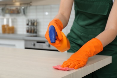 Photo of Female janitor cleaning table with rag in kitchen, closeup. Space for text