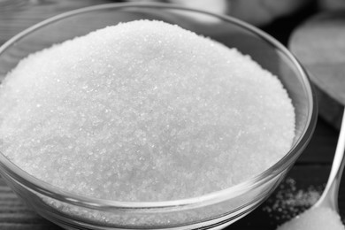 Photo of Granulated sugar in bowl on black table, closeup