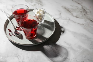 Photo of Delicious hibiscus tea, sugar cubes and dry roselle petals on white marble table, space for text