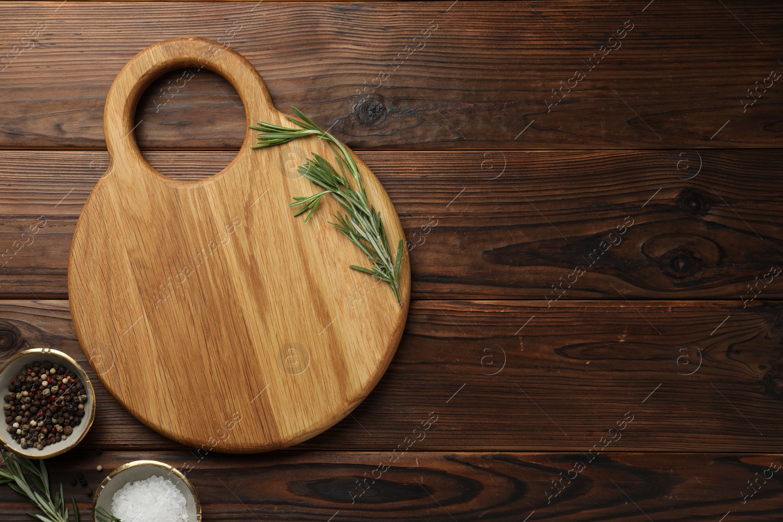 Photo of Cutting board, salt, pepper and rosemary on wooden table, flat lay. Space for text