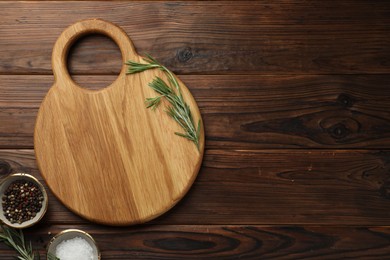 Photo of Cutting board, salt, pepper and rosemary on wooden table, flat lay. Space for text