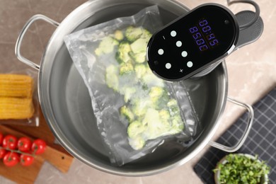 Photo of Thermal immersion circulator and vacuum packed broccoli in pot on grey marble table, flat lay. Sous vide cooking