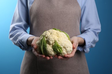 Woman holding fresh cauliflower against blue background, closeup