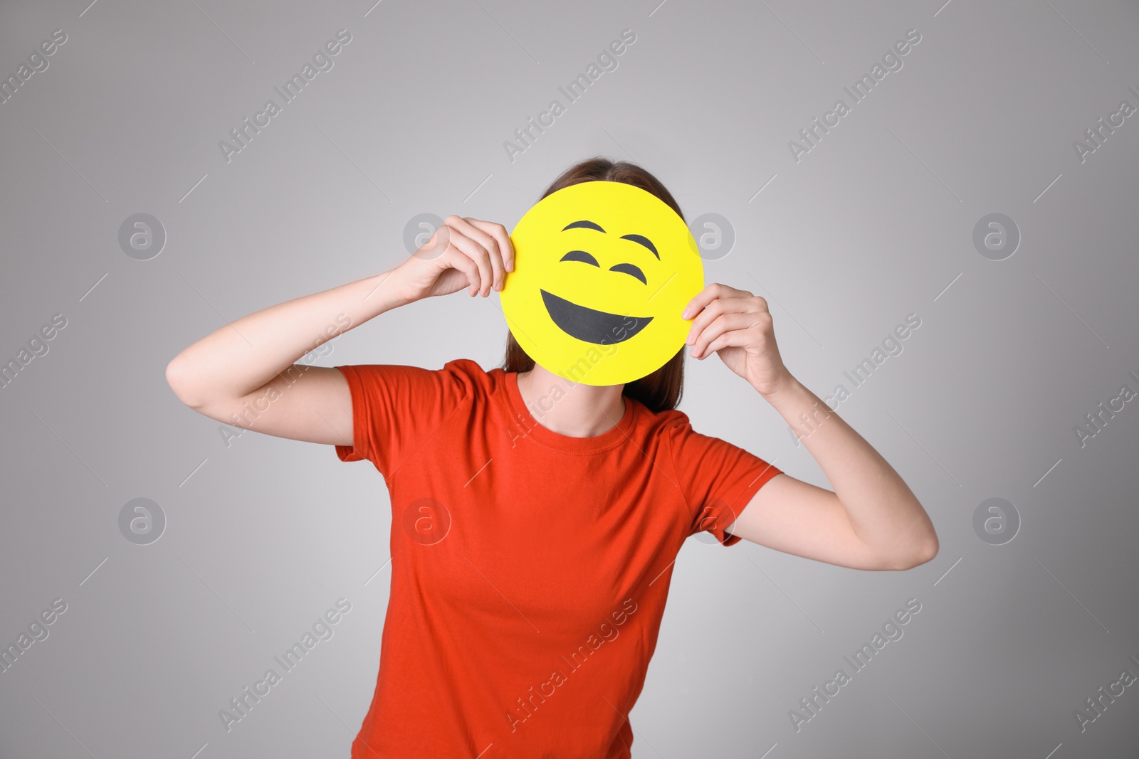 Photo of Woman covering face with laughing emoji on grey background