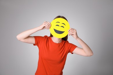 Woman covering face with laughing emoji on grey background