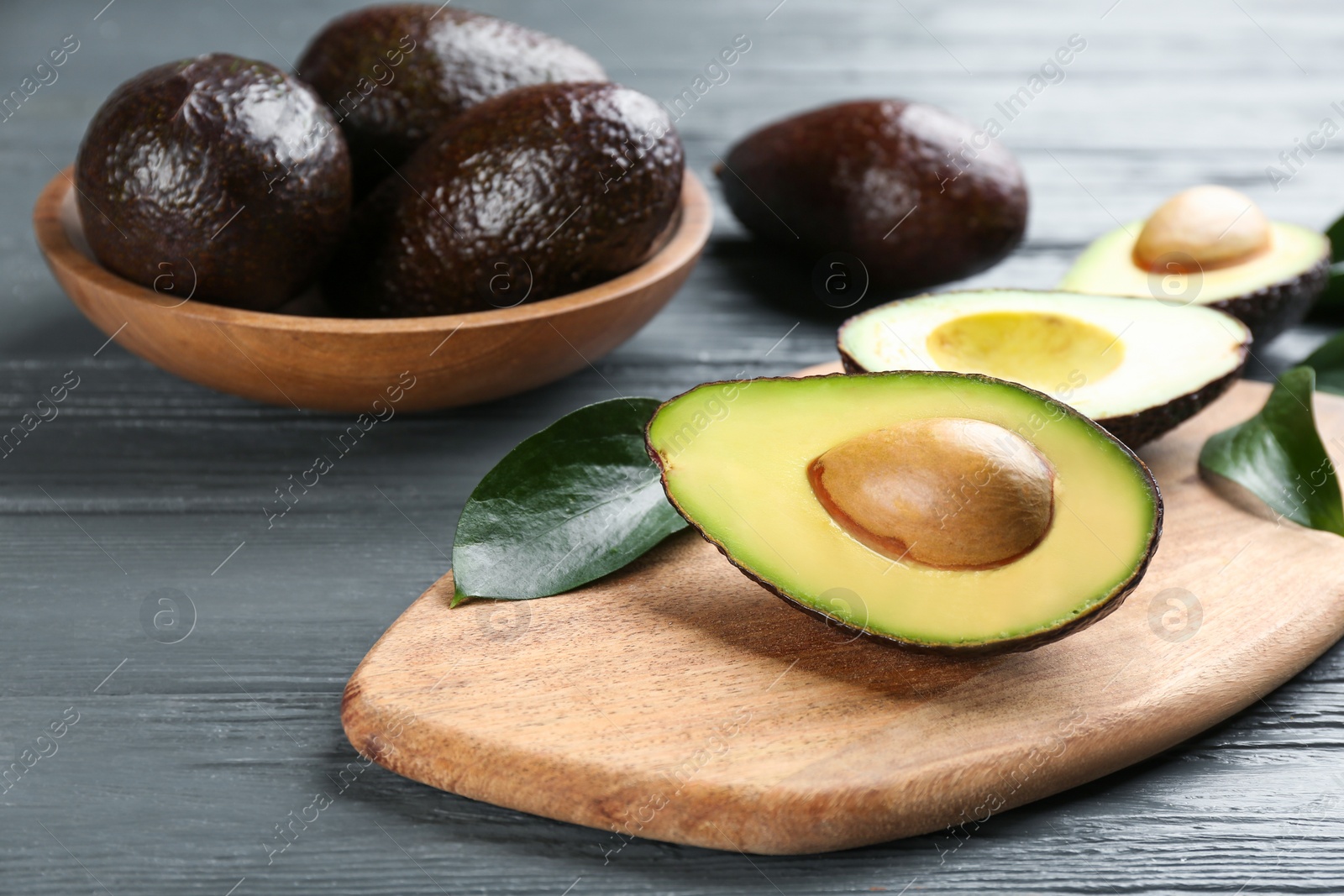 Photo of Whole and cut avocados on grey wooden table