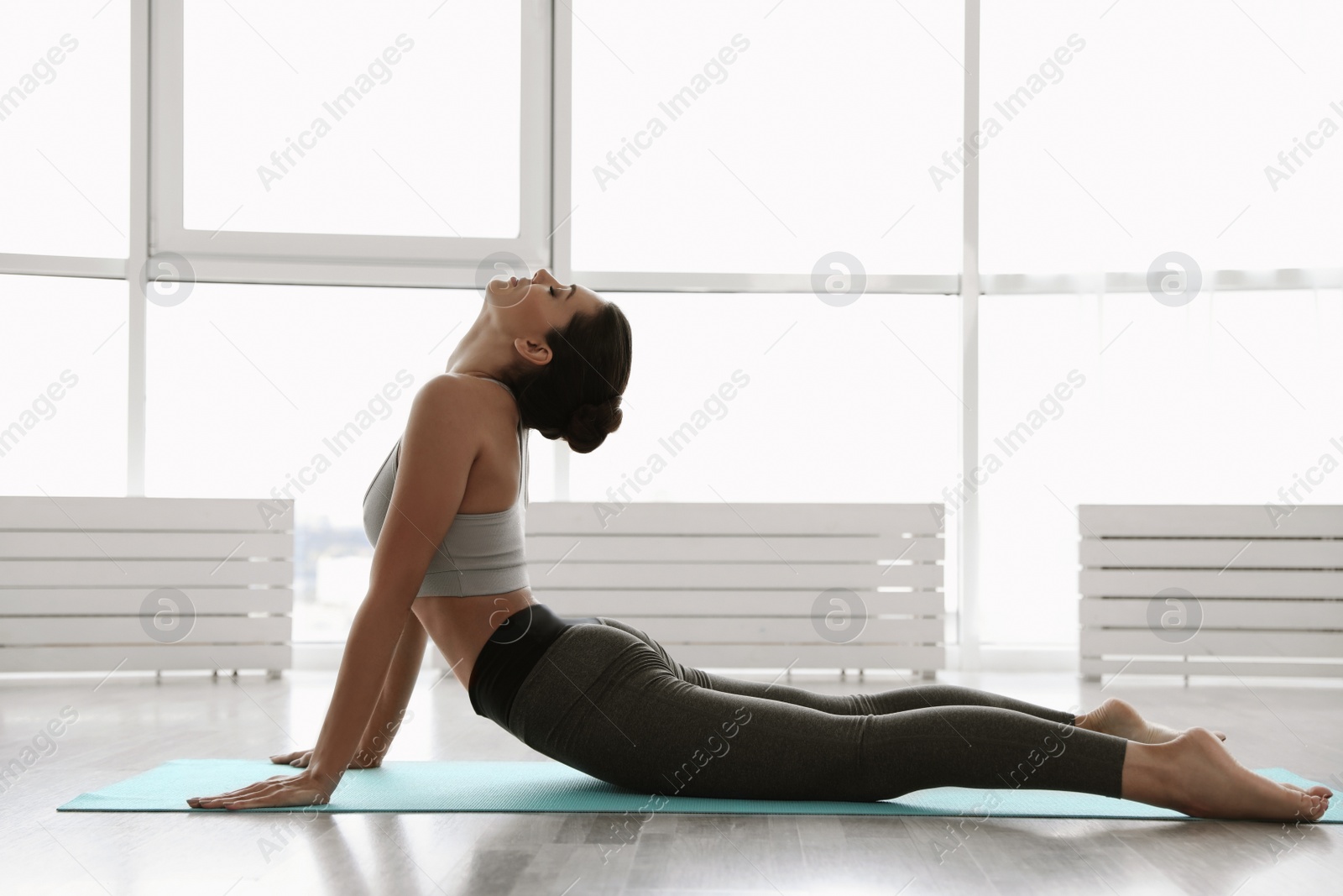 Photo of Young woman practicing high cobra asana in yoga studio. Bhujangasana pose