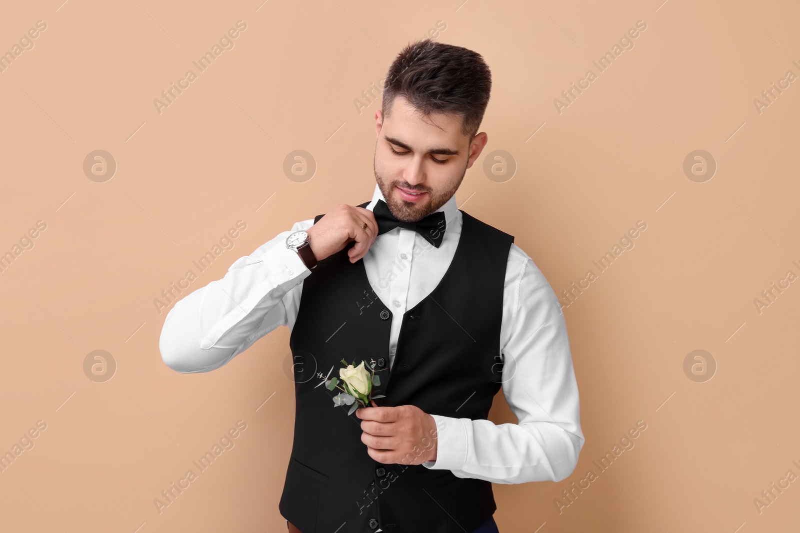 Photo of Handsome young groom with boutonniere on beige background. Wedding accessory