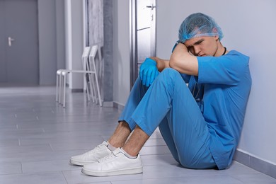 Photo of Exhausted doctor sitting near grey wall in hospital hallway