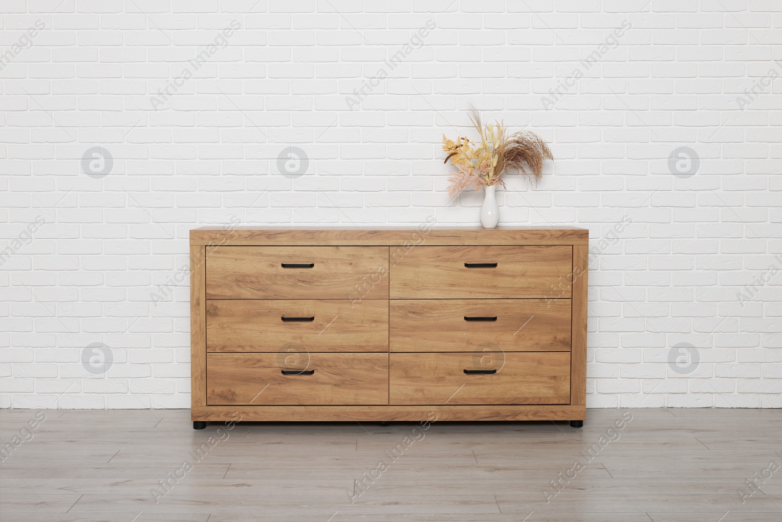 Photo of Wooden chest of drawers and vase near white brick wall. Interior design
