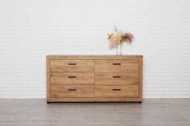 Wooden chest of drawers and vase near white brick wall. Interior design
