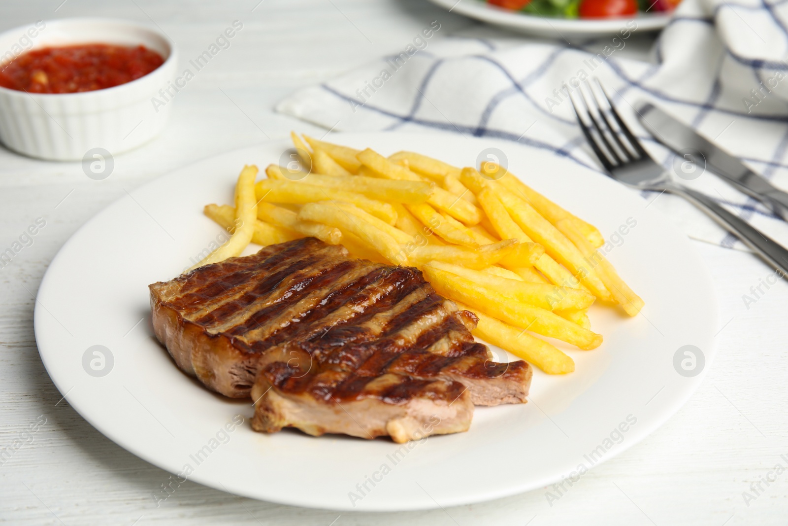 Photo of Tasty grilled beef steak and French fries on white wooden table