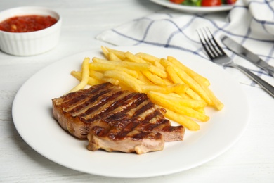 Tasty grilled beef steak and French fries on white wooden table