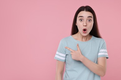 Photo of Portrait of surprised woman pointing at something on pink background. Space for text